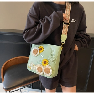 Detail of sunflower and white floral embroidery on light green crossbody bucket bag