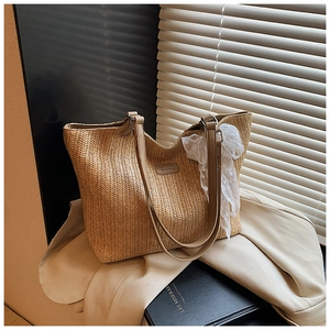 Detail of woven straw tote bag featuring leather straps and delicate white lace bow accent