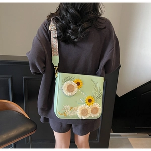 Detail of sunflower and white daisy embroidery on a light green leather bucket bag