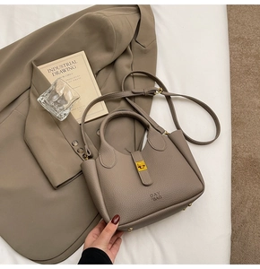 Detail of khaki lychee grain leather handbag with gold metal lock and studs on blazer
