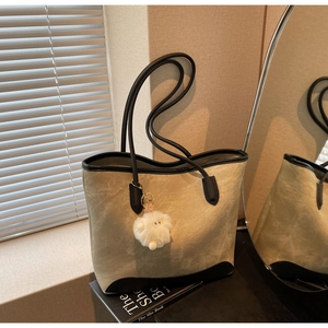 Detail of khaki suede tote bag with black leather trim and white fluffy charm accessory