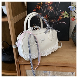 Detail of cream Boston bag with heart lace trim and bow charm on a wooden table