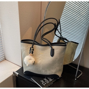 Detail of green suede tote bag with black leather trim, gold logo, and fluffy white pompom