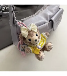 Brown plush bear keychain with bow and yellow sweater on a purple fashion handbag