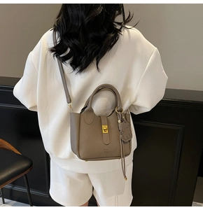 Detail of taupe pebbled leather tote with gold turn-lock and dog charm accessory