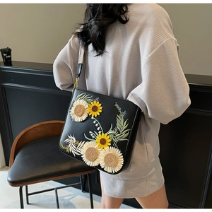 Detail of embroidered sunflower bucket bag featuring a wide canvas strap on model