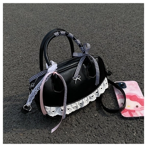 Close-up of shiny black bowling bag with lace trim and check ribbon bow on street