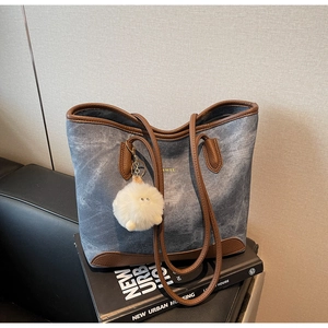 Detail of blue denim tote bag with brown leather trim and white fluffy pompom charm