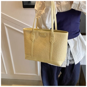 Détail d'un sac cabas jaune clair à texture tressée avec doubles anses et plaque de marque
