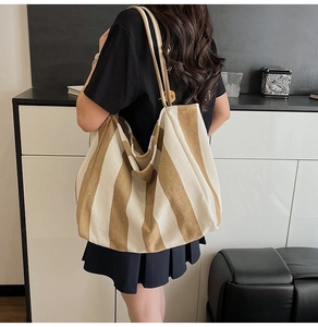 Detail of a large khaki and beige striped canvas tote bag worn by a model in a minimal setting
