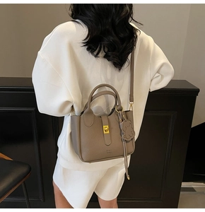 Detail of taupe pebbled leather shoulder bag with gold turn-lock and dog charm pendant