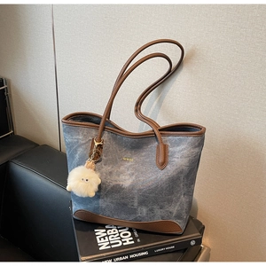 Detail of blue denim tote bag with brown leather trim and plush charm on a book