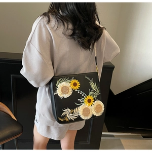 Detail of floral embroidery with sunflower and daisy patterns on a black bucket bag