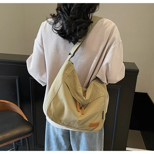 Detail showing oversized olive canvas messenger bag with brown leather brand tag on shoulder