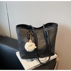 Detail of black matte tote bag with gold logo and a white plush lamb charm on a book