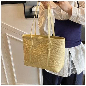 Détail du cabas jaune tressé avec lanières en cuir et plaque logo de marque en métal