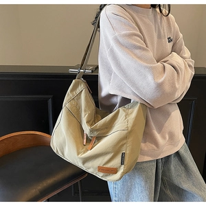 Close-up of khaki messenger bag with leather logo patch and adjustable shoulder strap