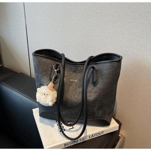 Detail of dark grey suede tote bag with gold logo and fluffy charm on books