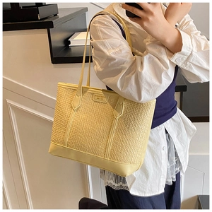 Détail d'un sac cabas beige clair avec texture en cuir tressé et plaque logo dorée