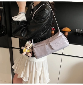 Detail view of light purple underarm bag with flap pockets and plush bear charm accent