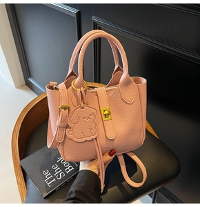 Detail of pink pebbled leather handbag with gold twist lock and cute dog charm on black seat