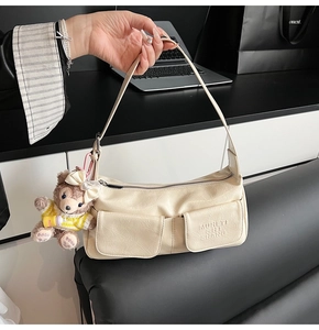 Detail of cream white faux leather shoulder bag featuring two front pockets and plush charm