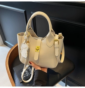 Close-up of creamy white lychee grain leather bag with gold clasp and dog charm