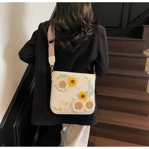 Detail of white crossbody bucket bag with floral embroidery and colorful wide strap