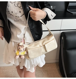 Detail of beige pleated shoulder bag with front flap pockets and plush pendant