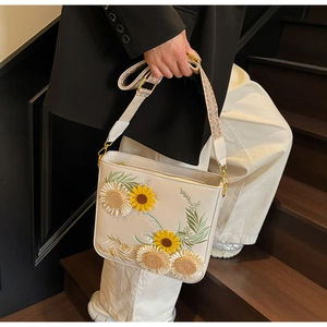 Detail of sunflower embroidery on off-white leather bucket bag with jacquard strap