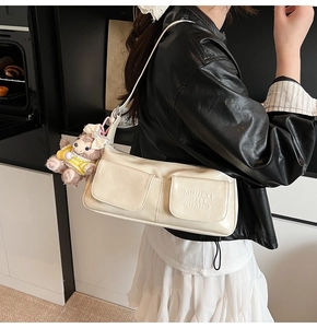 Detail of cream glossy faux leather shoulder bag with two front pockets and plush bear charm