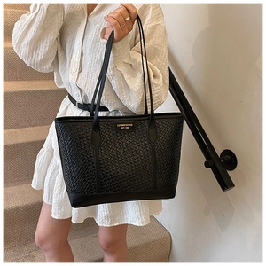 Détail de la texture tressée sur grand sac cabas noir porté avec robe blanche plissée