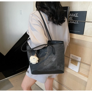 Detail of dark grey tote bag with black leather trim and white plush toy pendant