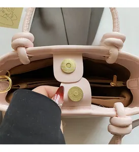 Detail view of pink bucket bag showing magnetic metal clasp, inner zipper pocket and knot handle