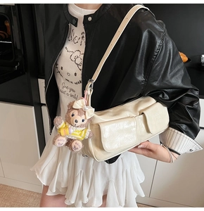 Detail of cream white PU leather crossbody bag with dual pockets and plush charm on model