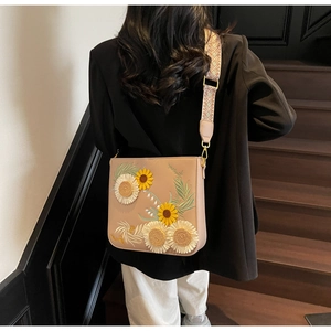 Detail of sunflower embroidery on beige shoulder bag with geometric jacquard strap