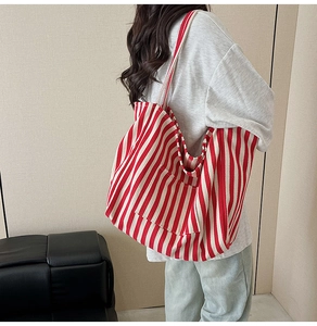 Detailed view of a large red and white striped canvas tote bag worn on a person's shoulder