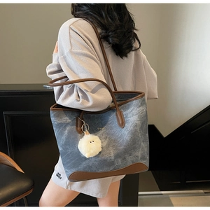 Detail of blue denim tote bag with brown leather trim and cute plush charm on shoulder
