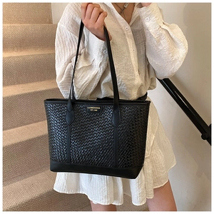 Détail du sac cabas en cuir tressé noir avec plaque métallique sur escalier beige