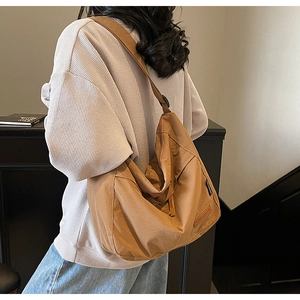 Brown canvas hobo crossbody bag with wide strap and side label shown on a model