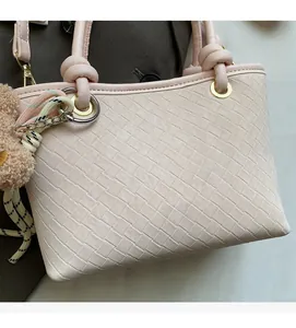 Close-up of pink woven texture handbag with brand logo, metal rings and teddy bear charm