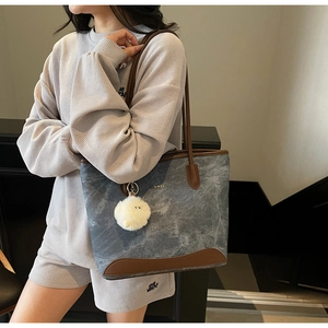 Detail of blue tote bag with brown leather trim and fluffy white keychain charm