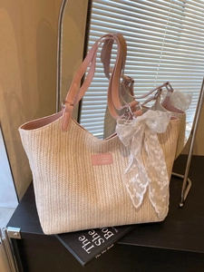 Woven straw tote bag with pink handles and large white lace bow in a minimalist setting