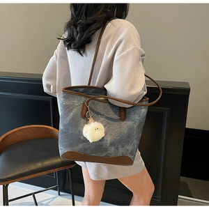 Detail of blue denim tote bag with leather trim and white plush ball charm on a model