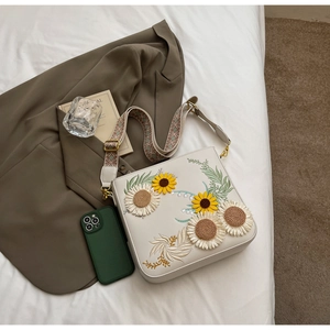 Detail of white crossbody bag featuring sunflower embroidery and a retro floral strap