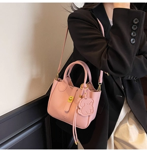 Pink lychee texture leather tote bag with dog charm shown on shoulder by model