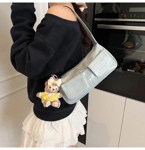Detail of light blue faux leather baguette bag with side pocket and teddy bear charm