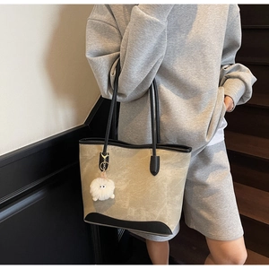 Detail of beige tote bag with black leather handles and a plush eyeball charm