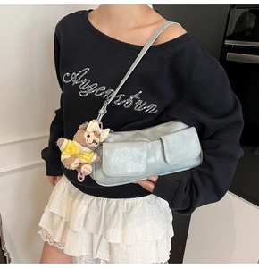 Detail of light blue shoulder bag featuring double front pockets and a cute bear charm