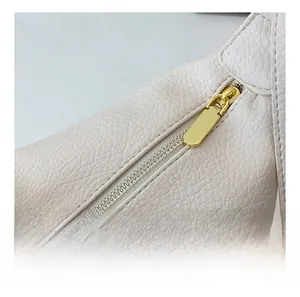 Detail of smooth gold-tone zipper on textured cream leather saddle bag